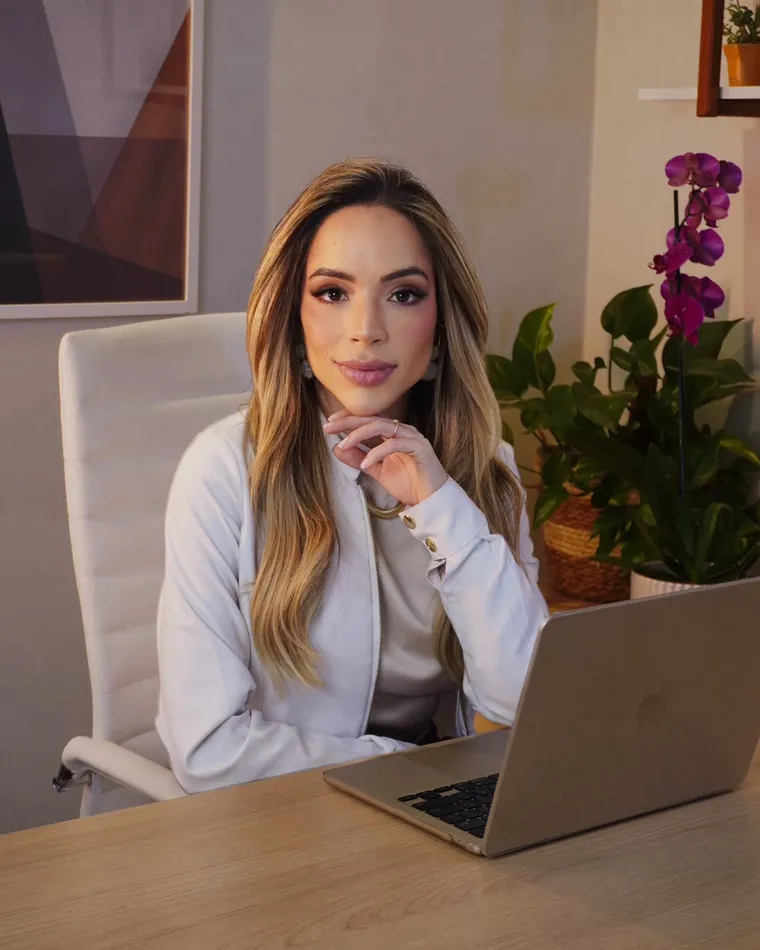 Dra. Ana Paula Souza sentada à mesa do consultório, com o notebook aberto